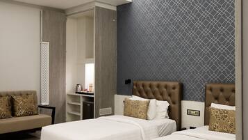 A hotel room with a bed, a desk, and a chair. There is a wardrobe and a mirror.