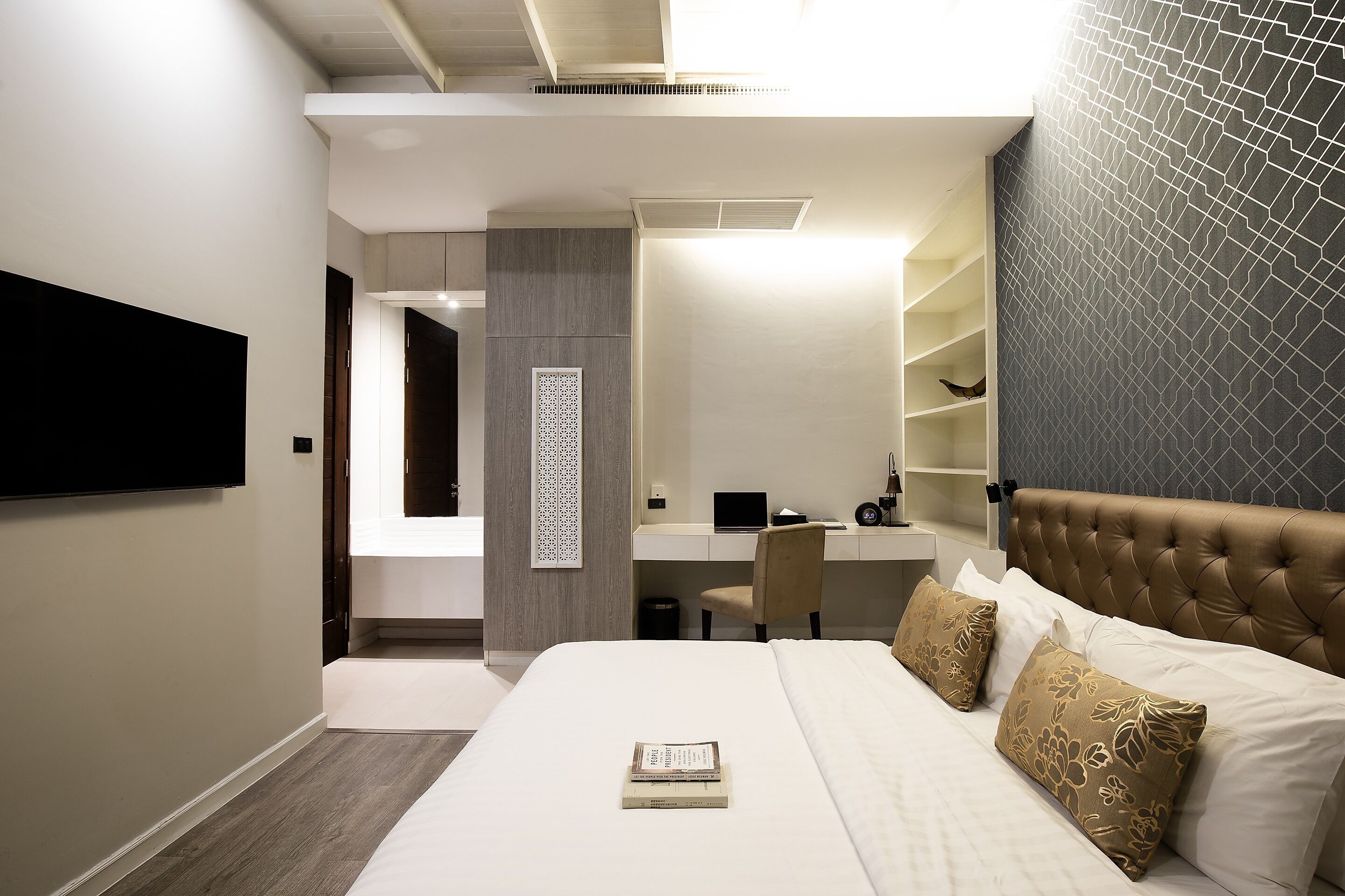 A modern bedroom with a large bed, a desk, and a television mounted on the wall.