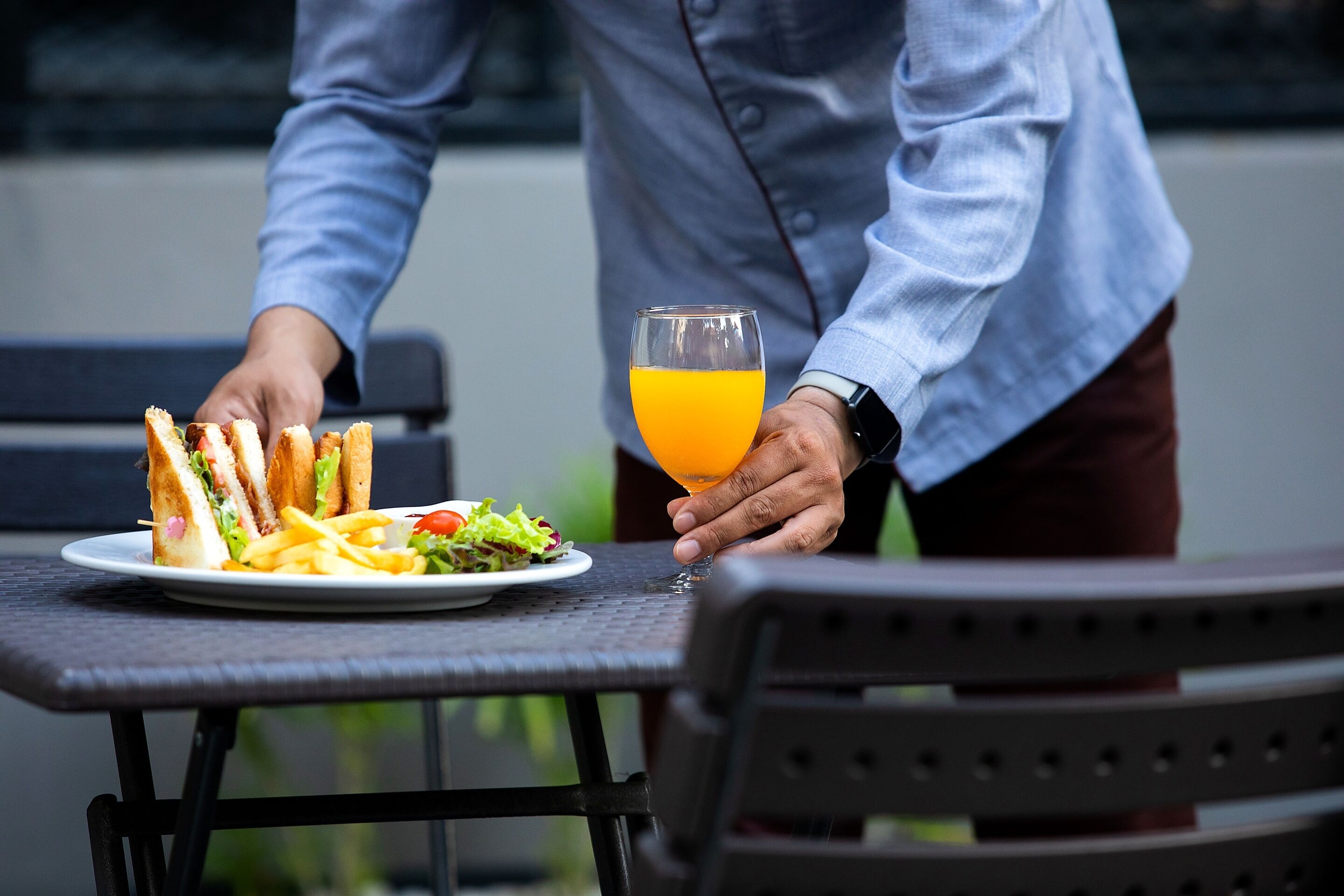 A person serving a plate of food and a glass of orange juice on an outdoor table.