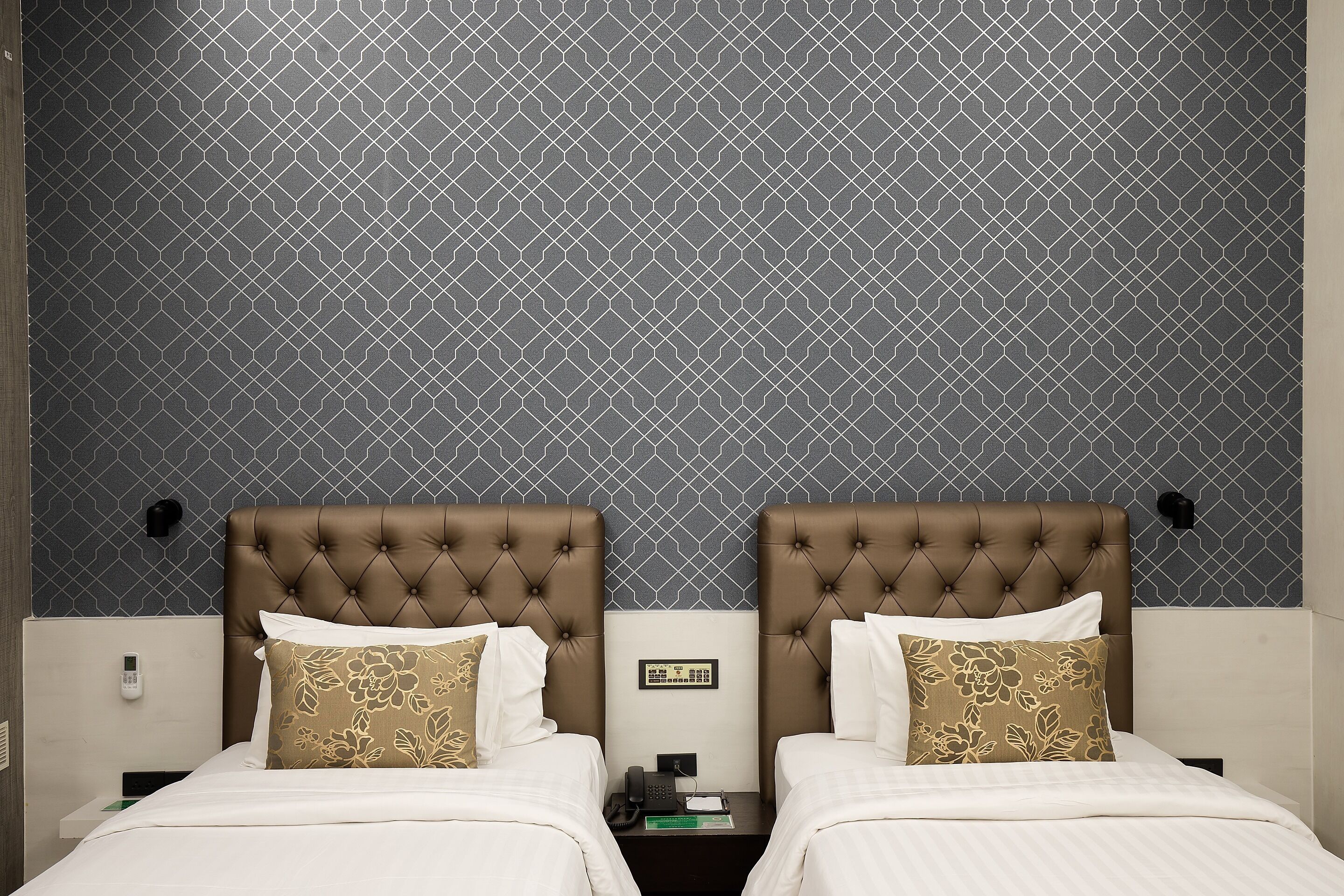 Een hotelkamer met twee bedden, een kamer met een patroon en een telefoon op het nachtkastje.