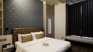 A hotel room with a large bed, a bedside table with a phone and a book, a window with curtains, and a wall with a geometric pattern.