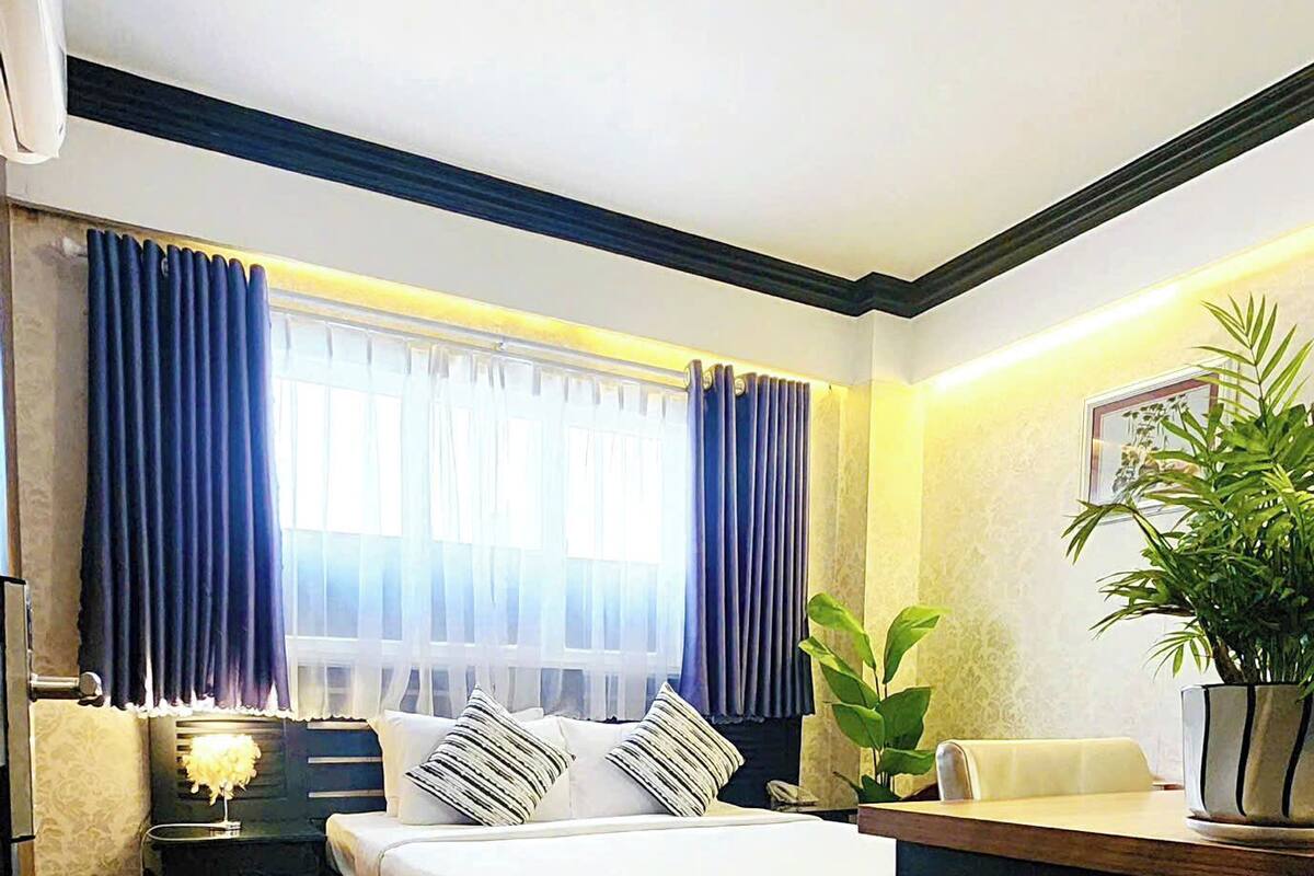 A bedroom with a bed, bedside tables, a desk, and a potted plant.