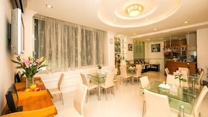 A modern dining area with glass tables and chairs, a wooden counter, and a large window with curtains. - Rosa Hotel & Spa (Ho Chi Minh City)