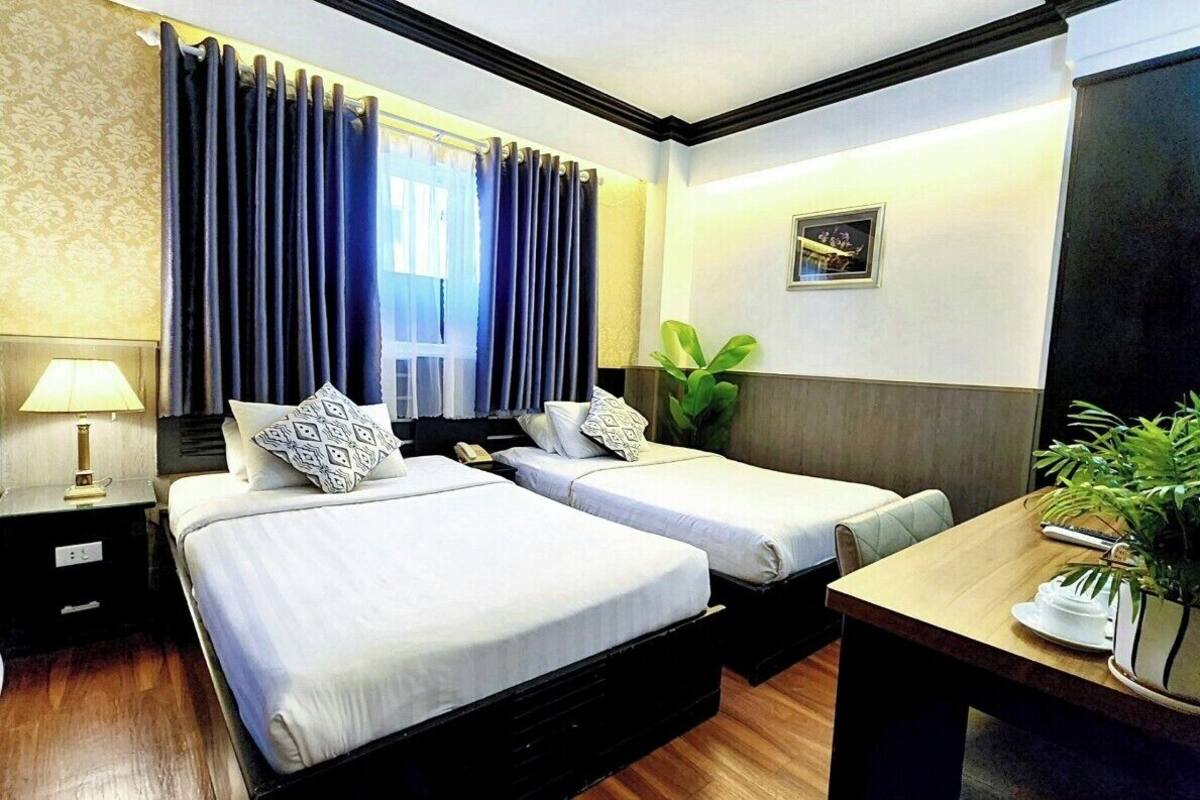A hotel room with two beds, a bedside table with a lamp, a small table with a plant, and a picture on the wall.