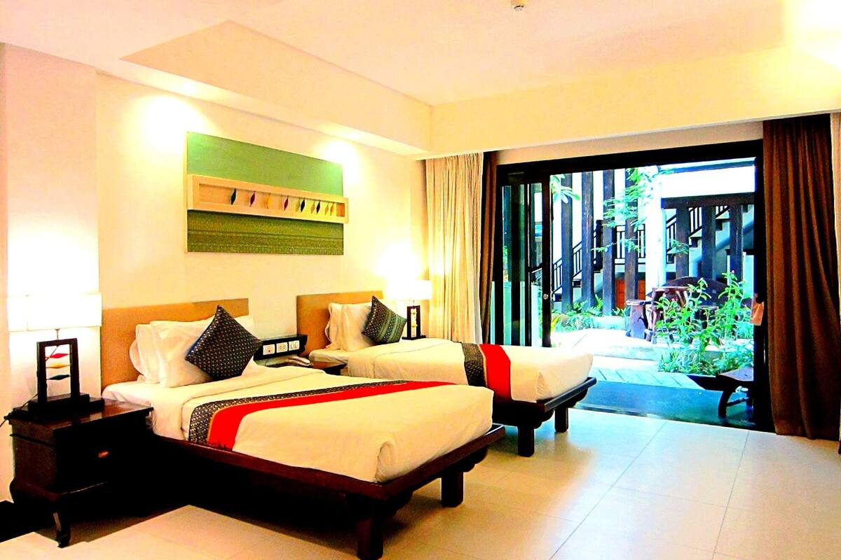 A hotel room with two beds, a large window, and a view of the outdoor area.