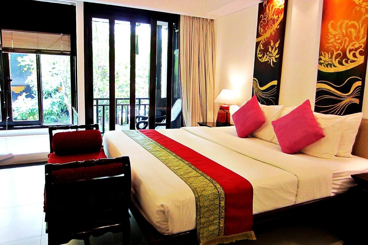 A hotel room with a large bed, a chair, a nightstand, and a window with curtains.