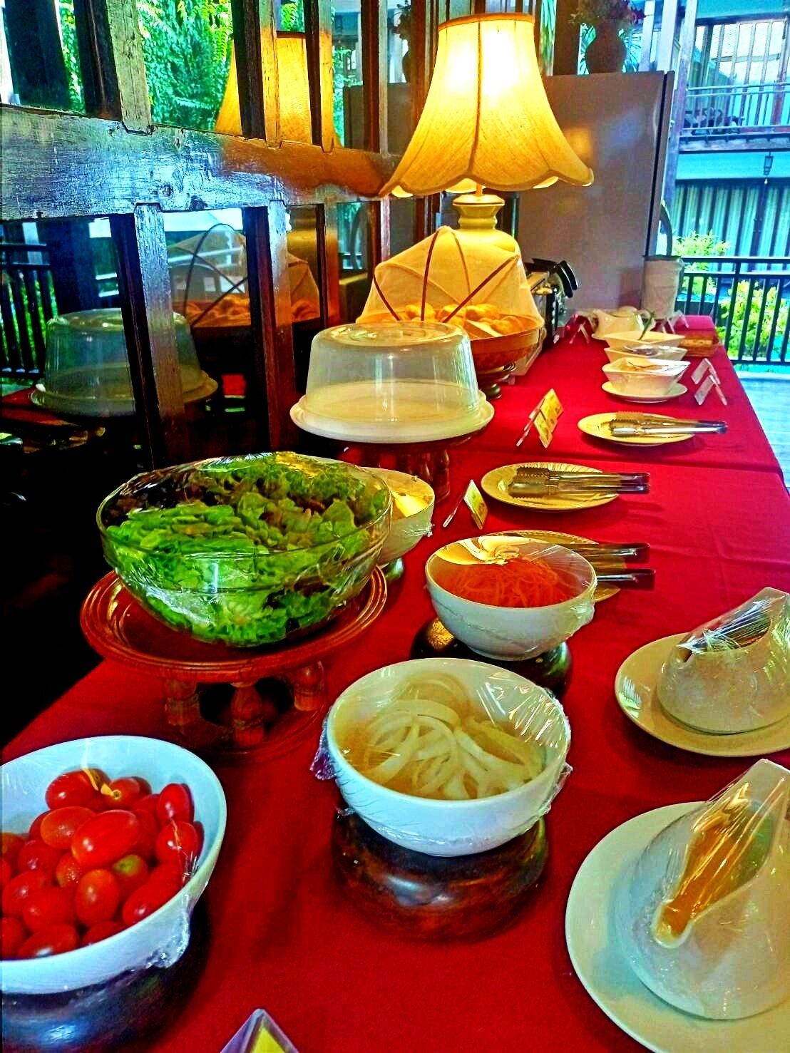 A buffet table with various dishes and utensils, covered with a red tablecloth.