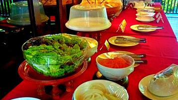 A buffet table with various dishes and utensils, covered with a red tablecloth.