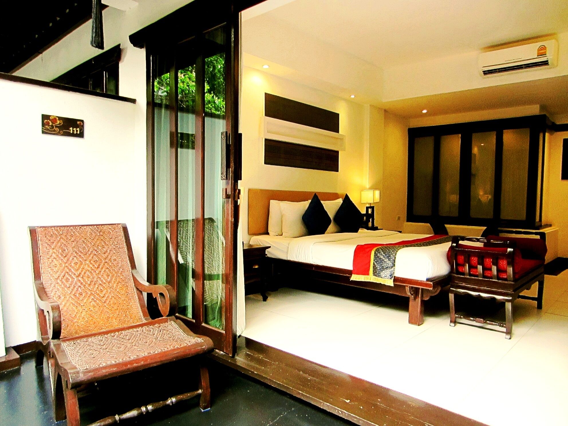 Habitación de hotel con cama, una silla, una mesita y puerta corrediza de vidrio que da a un espacio exterior.