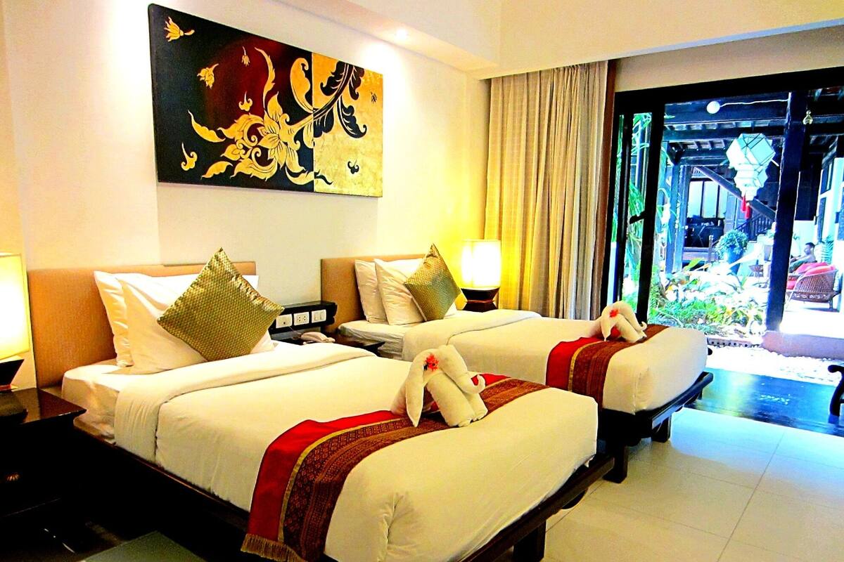 A hotel room with two beds, a large decorative painting, a window with curtains, and a view of the outside.