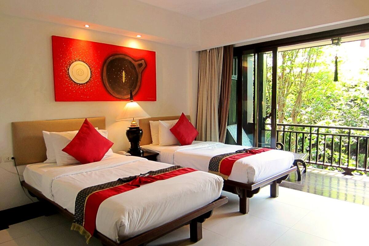 A hotel room with two beds, a large window, and a red artwork on the wall.