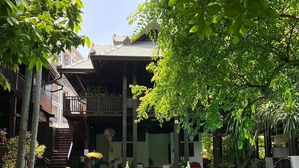 Et poolområde med klart vand, omgivet af frodig vegetation og en bygning med balkon.