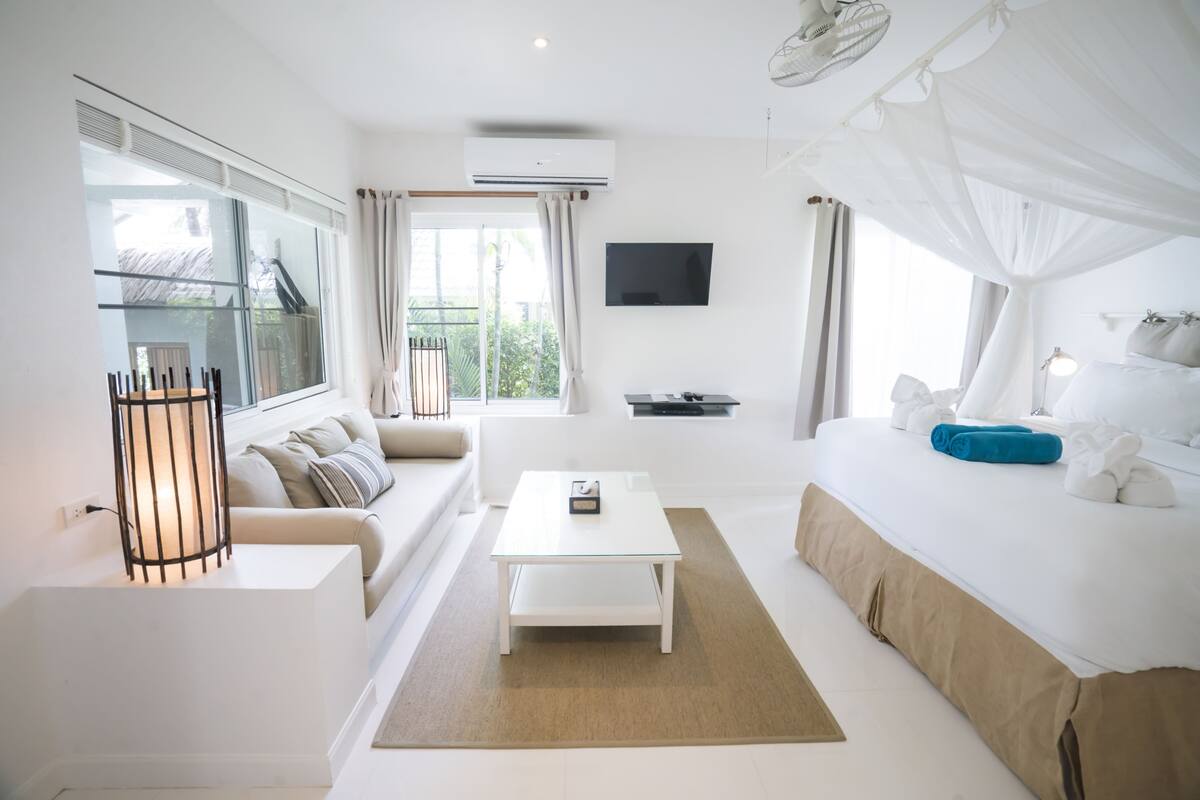 Ein modernes Hotelzimmer mit einem großen Bett, einer Couch, einem Couchtisch, einem Fernseher und einer Klimaanlage.