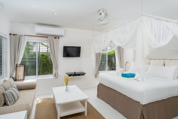 A bedroom with a bed, a TV, a white table, and a window with curtains.