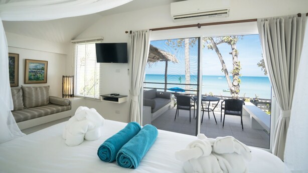 A hotel room with a bed, a sofa, a TV, and a balcony with a view of the sea. - King's Garden Resort (Koh Samui)