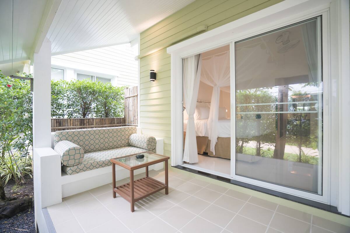 Eine Terrasse mit einem weißen Sofa, einem Glastisch und einer Glasschiebetür, die zu einem Schlafzimmer führt.