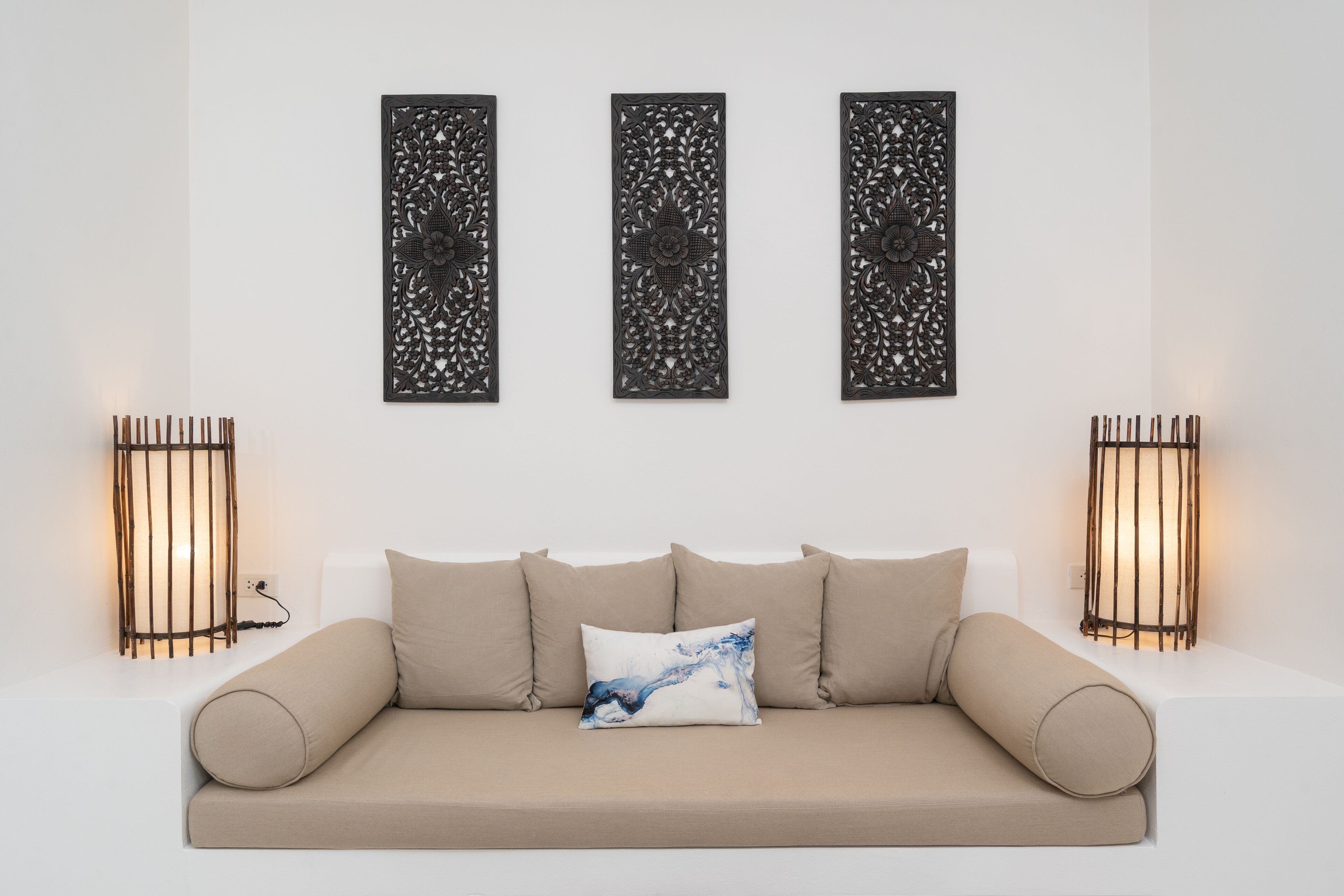 A modern living room with a beige sofa, three decorative wall panels, and two wall-mounted lamps.