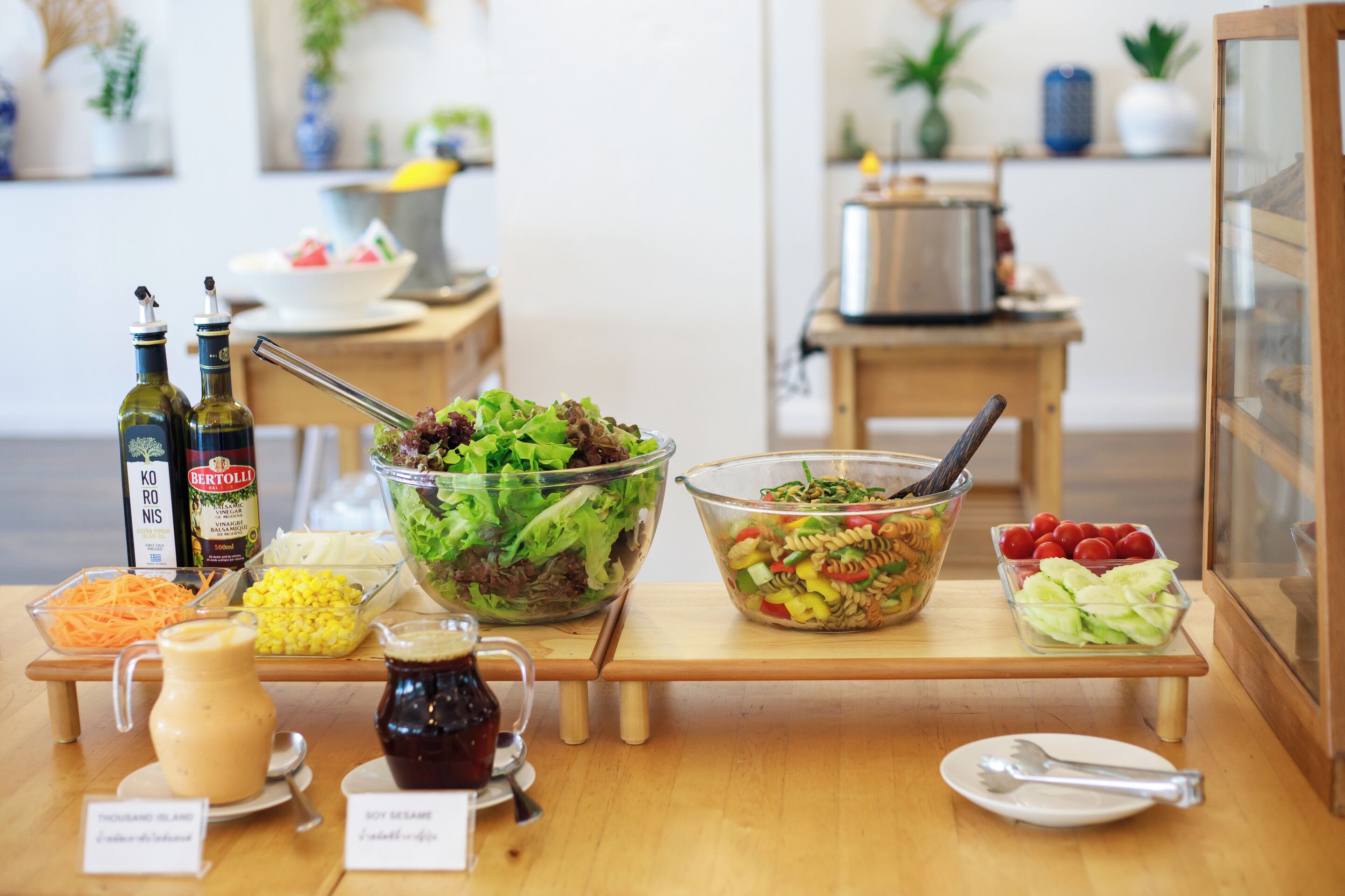 A buffet table with various dishes, including salads, pasta, and a bowl of fruit. There are also condiments and a pitcher of sauce.