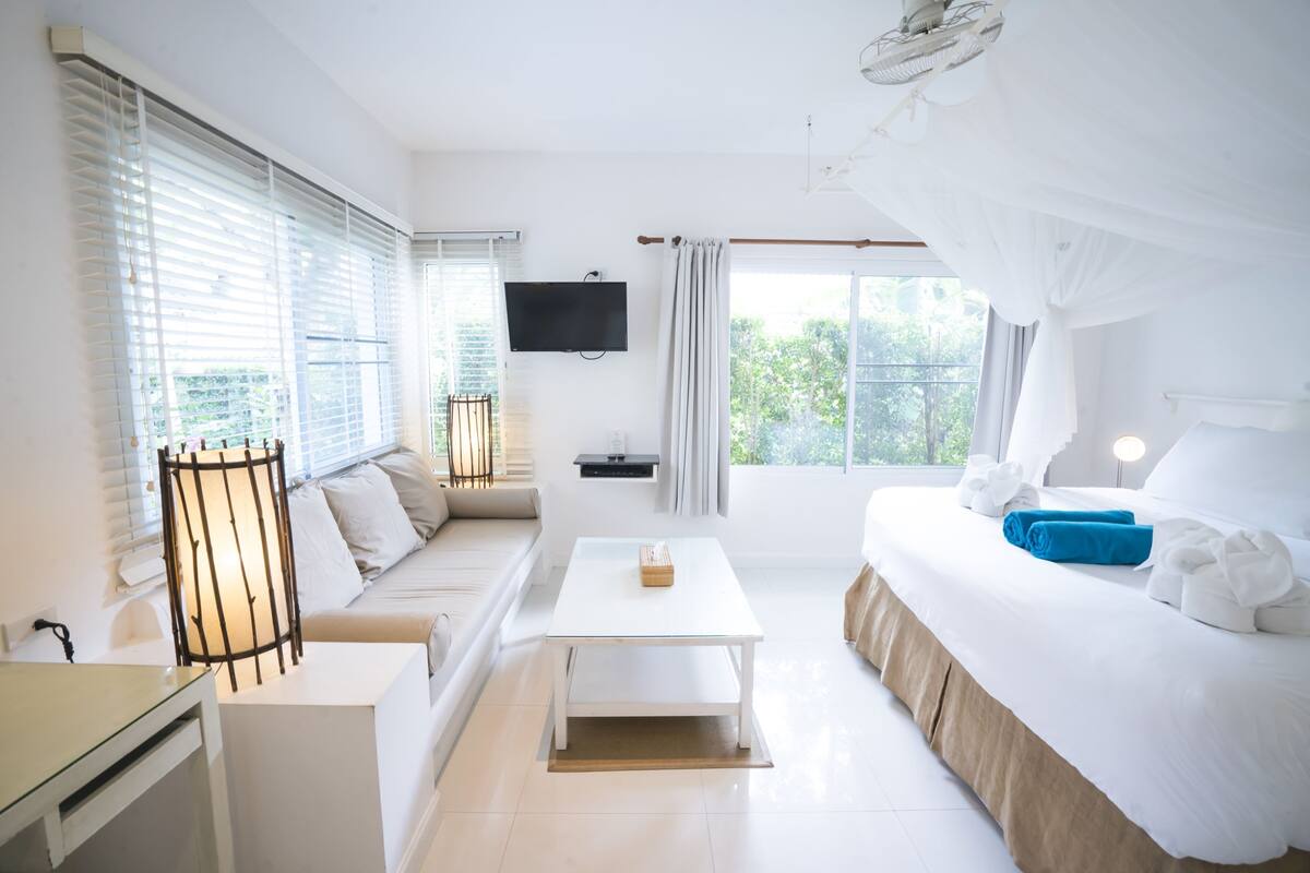 Ein Hotelzimmer mit Bett, einer Couch, einem Fernseher und einem Fenster mit Jalousien.