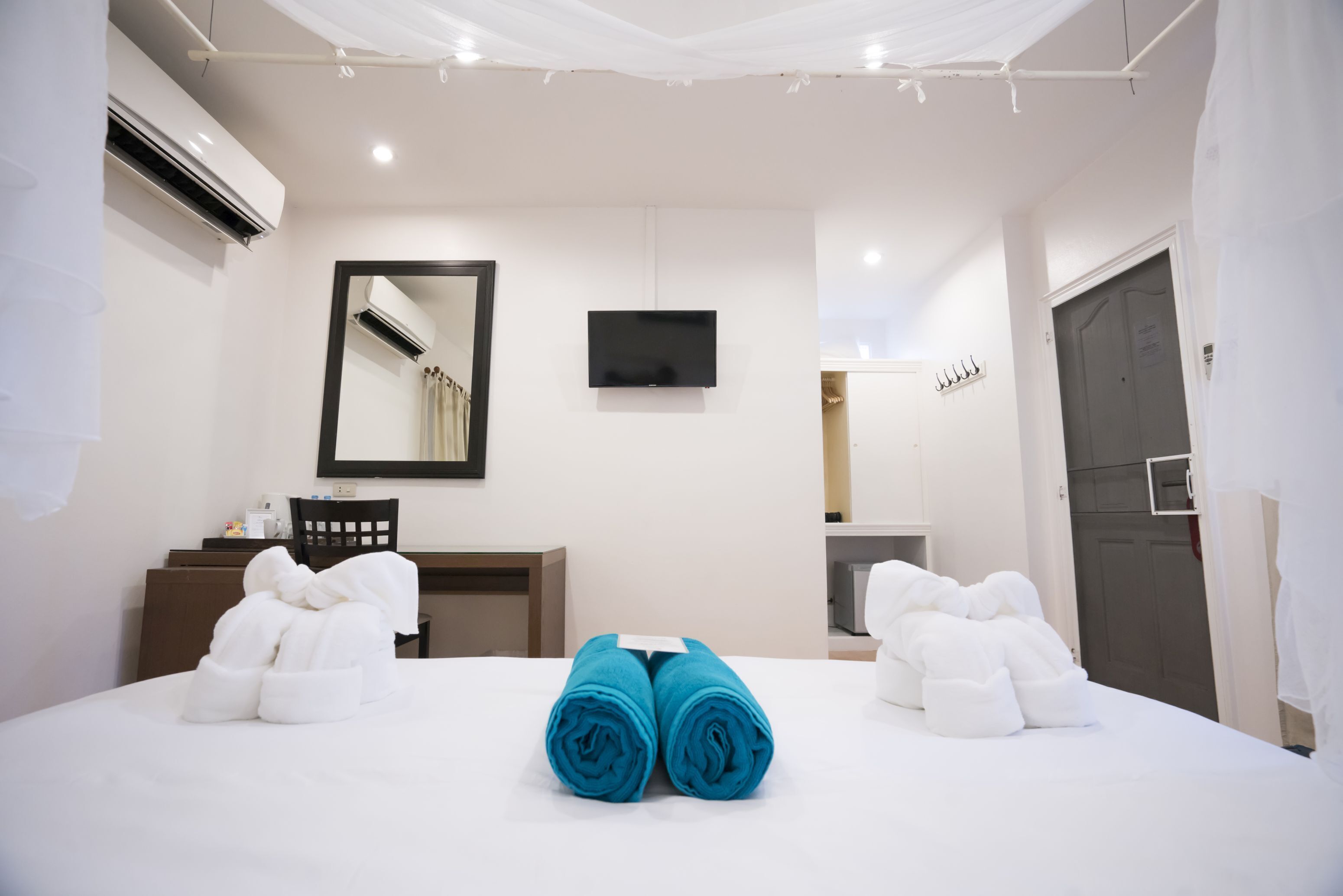 A hotel room with a bed, a desk, a chair, a TV, and a wardrobe.