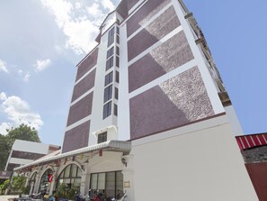 A tall hotel with a white facade and brown accents, featuring a large arched entrance and multiple windows.
