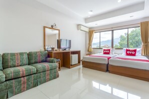 A hotel room with a green sofa, a bed with red pillows, a TV, and a large window with a view of mountains.