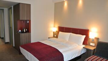 A hotel room with a large bed, two bedside lamps, a red headboard, a wooden wardrobe, and a red and white striped chair.