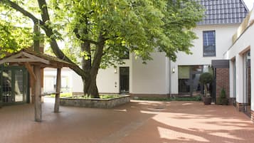 A courtyard with a large tree, a wooden bench, and a building with a tiled roof.
