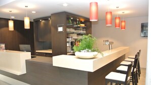 A modern bar area with a white countertop, bar stools, and a potted plant. - Hotel zur Krone (Gescher)