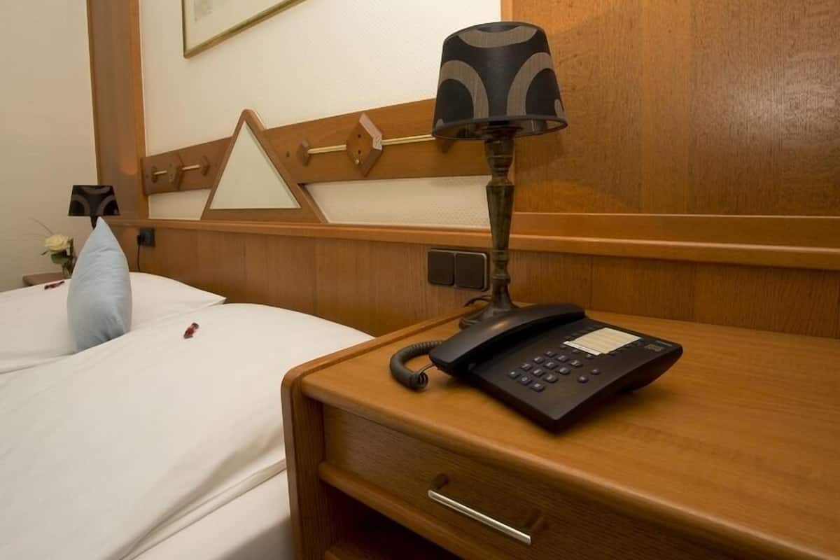 A hotel room with a wooden headboard, a bedside lamp, a telephone, and a small table with a vase of flowers.