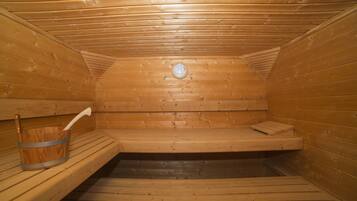 Una sauna con paredes y bancos de madera, un banco en el centro, y un cubo con un cepillo a la izquierda.