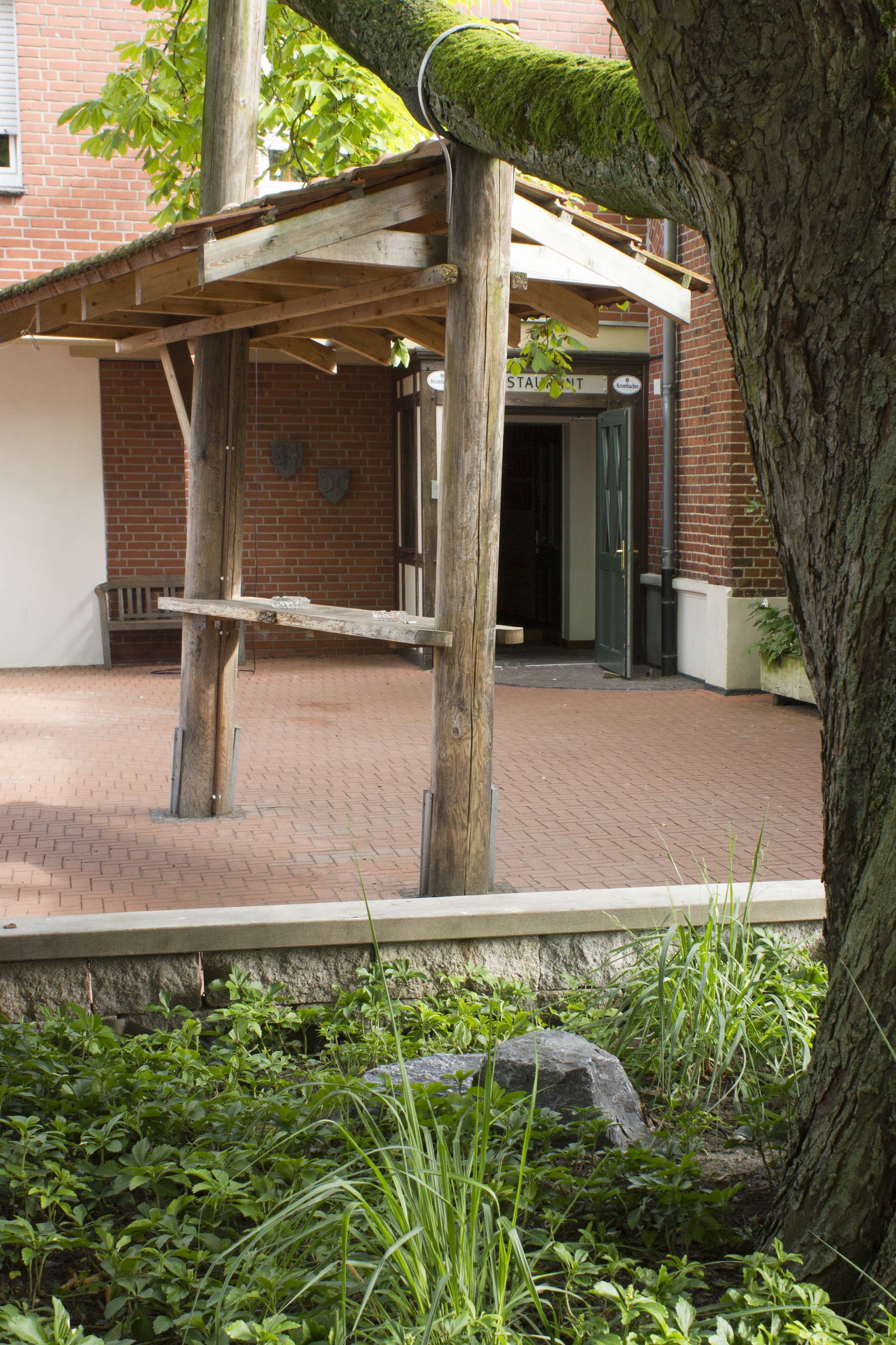 Una estructura de pérgola de madera con un edificio de ladrillo al fondo.
