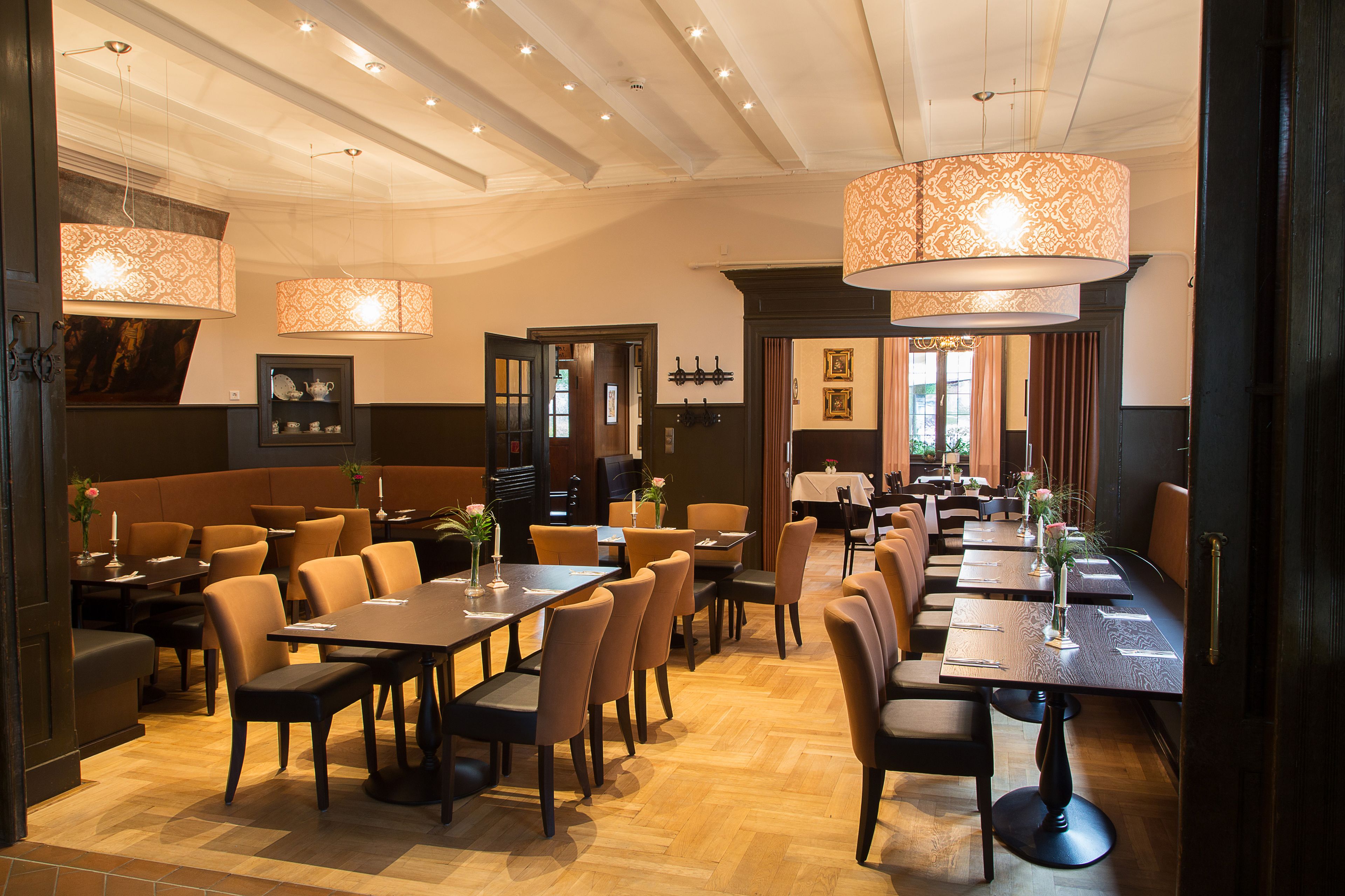 A restaurant with multiple dining tables and booths, wooden flooring, and pendant lighting.