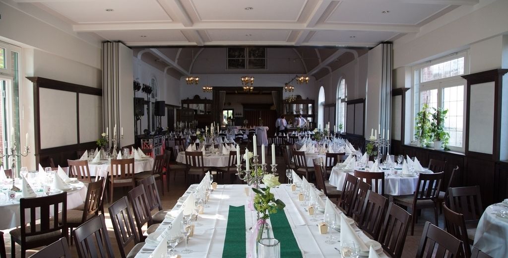 Un amplio salón de banquetes con largas mesas dispuestas para un evento formal, con candelabros y una alfombra verde que marca el pasillo.