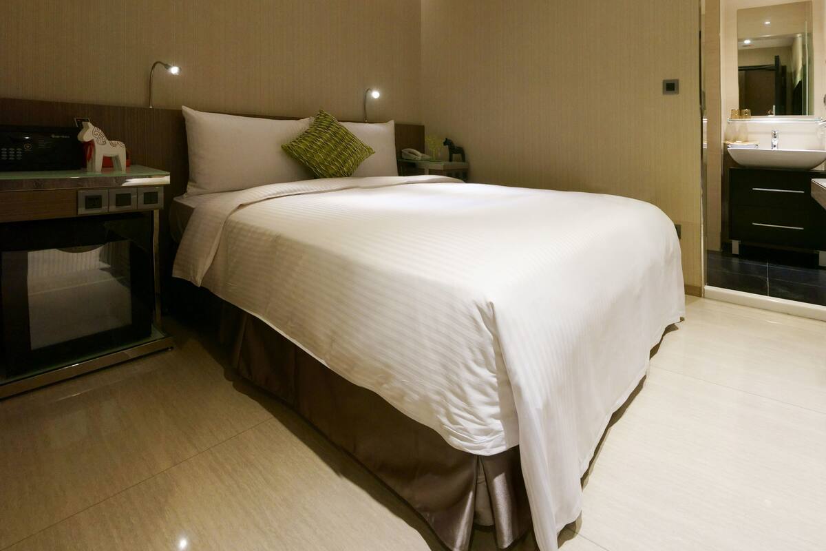 Hotelkamer met een groot bed, een bureau met telefoon en een badkamer met wastafel en spiegel.