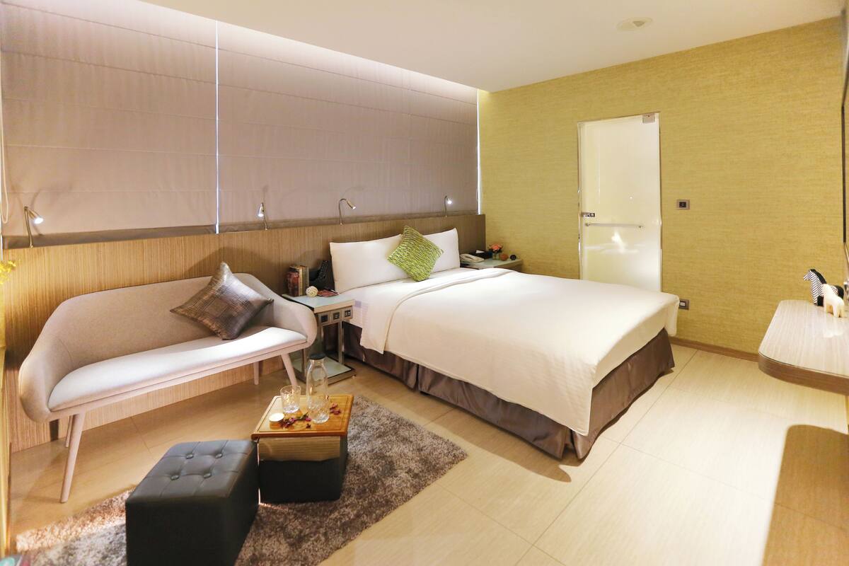 Een hotelkamer met een bed, een bank, een kleine tafel met een lamp, en een nachtkastje met een telefoon en een vaas.
