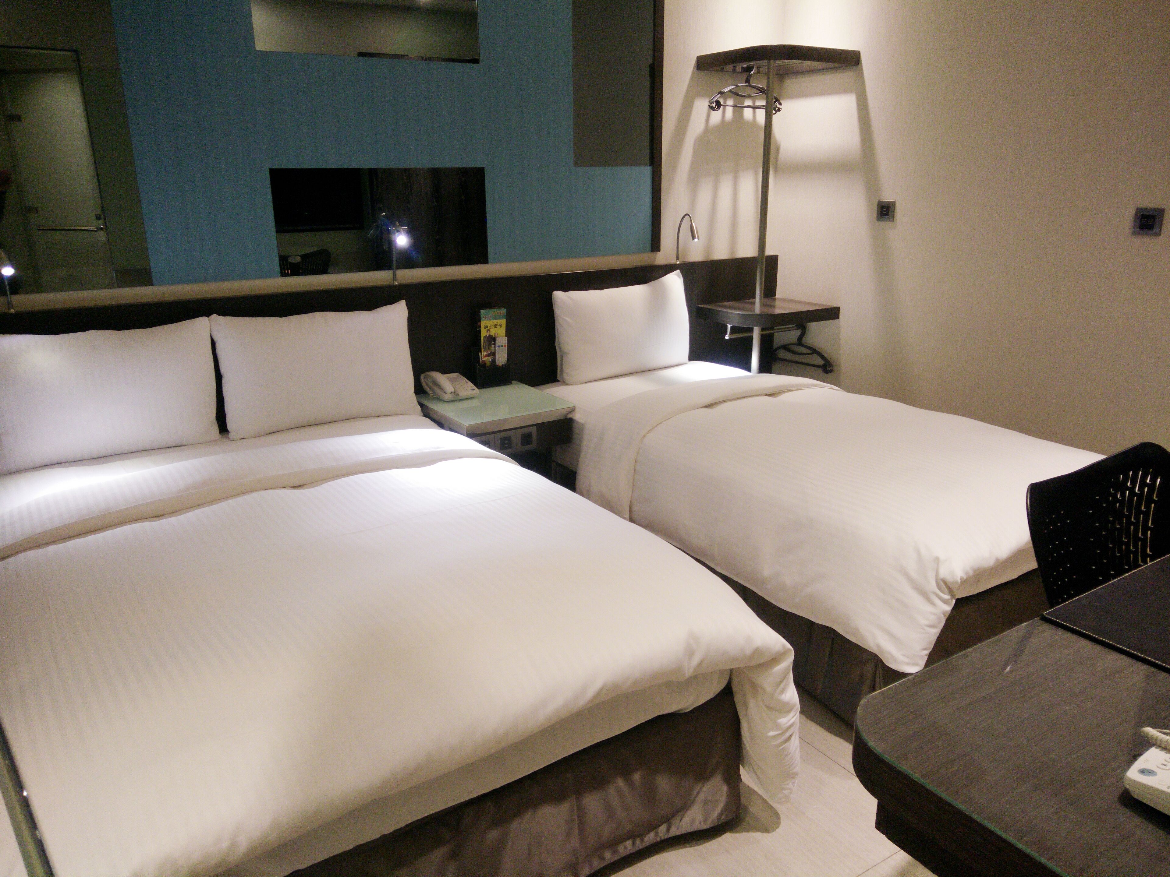 A hotel room with two beds, a desk, a lamp, and a telephone.