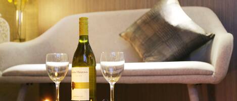 A bottle of wine and two glasses on a tray, with a candle and flowers on a table in a cozy room with a sofa and a pillow.