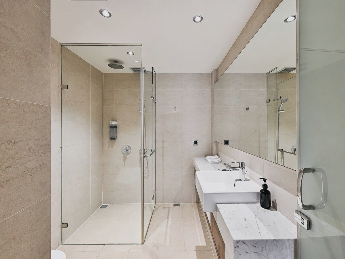 A modern bathroom with a glass-enclosed shower, a vanity with a mirror, and a marble countertop.