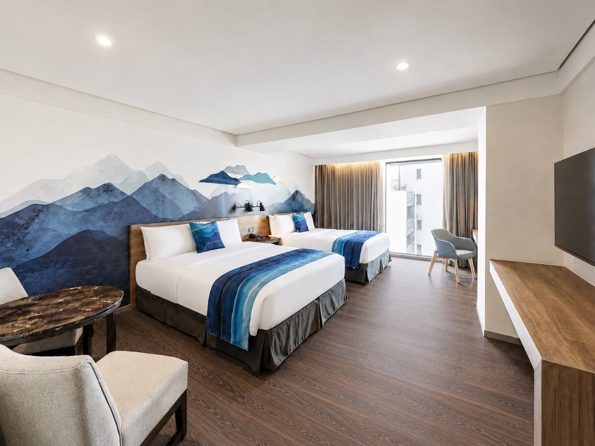 A hotel room with two beds, a desk, a chair, and a large TV.