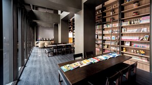 A modern library with a long table displaying books and magazines, surrounded by bookshelves filled with various books and decorative items. - Just Sleep Hualien Zhongzheng (Hualien City)