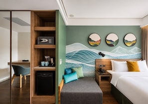 Habitación de hotel con cama, mesita de noche, escritorio, silla y una pared decorada con obras de arte.