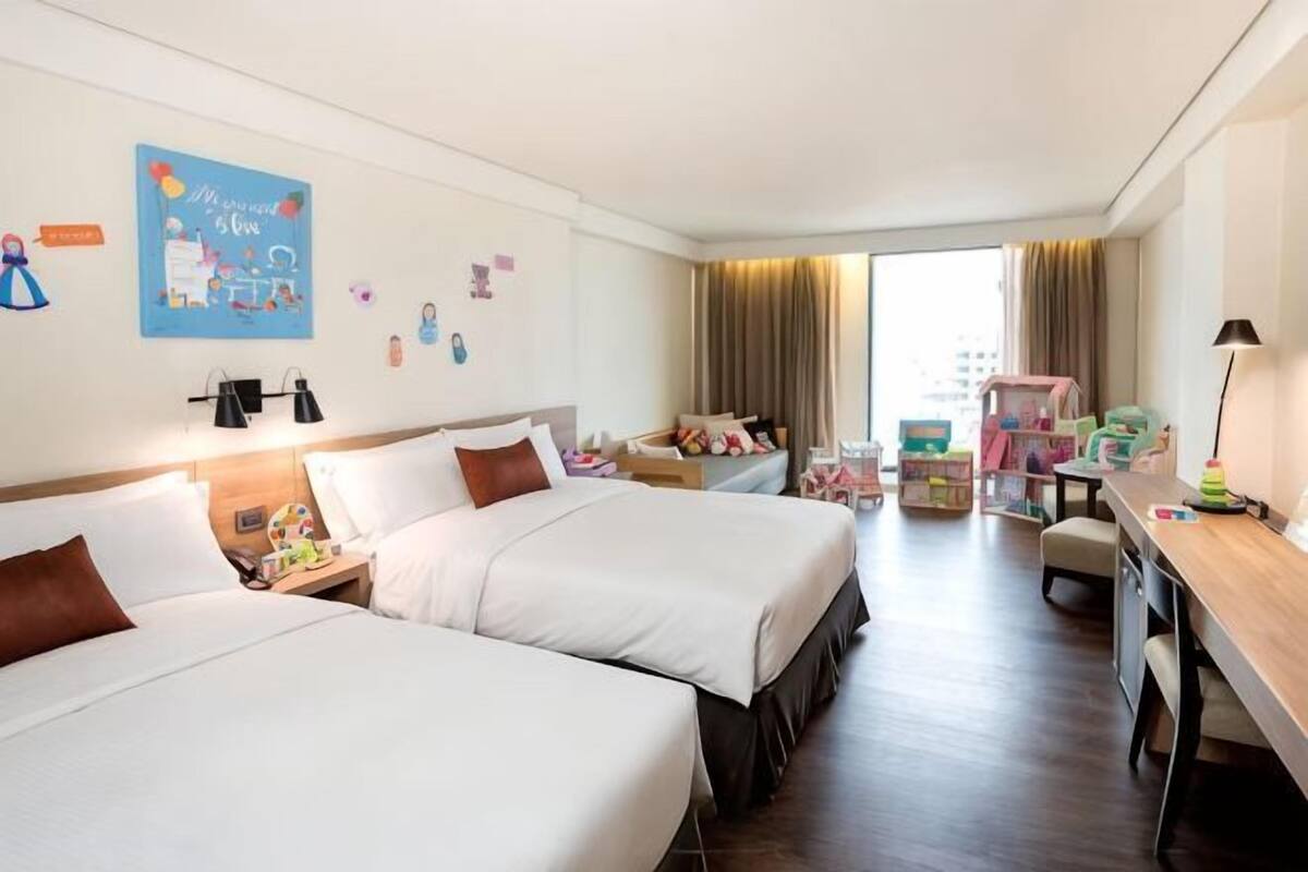 A hotel room with two beds, a desk, a chair, and a window with curtains.