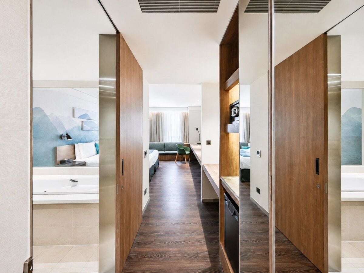 A hotel corridor with a bed, a desk, and a bathroom.
