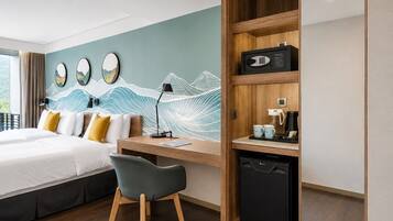 Quarto de hotel com cama, escrivaninha, cadeira e uma parede com obras de arte.