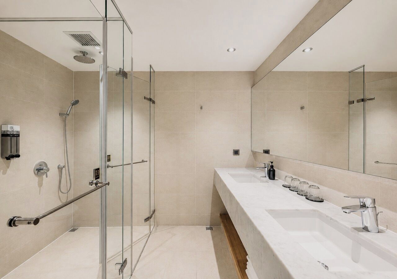 Une salle de bain moderne avec une douche à l’italienne en verre, un long meuble-lavabo doté de plusieurs vasques et un grand miroir.