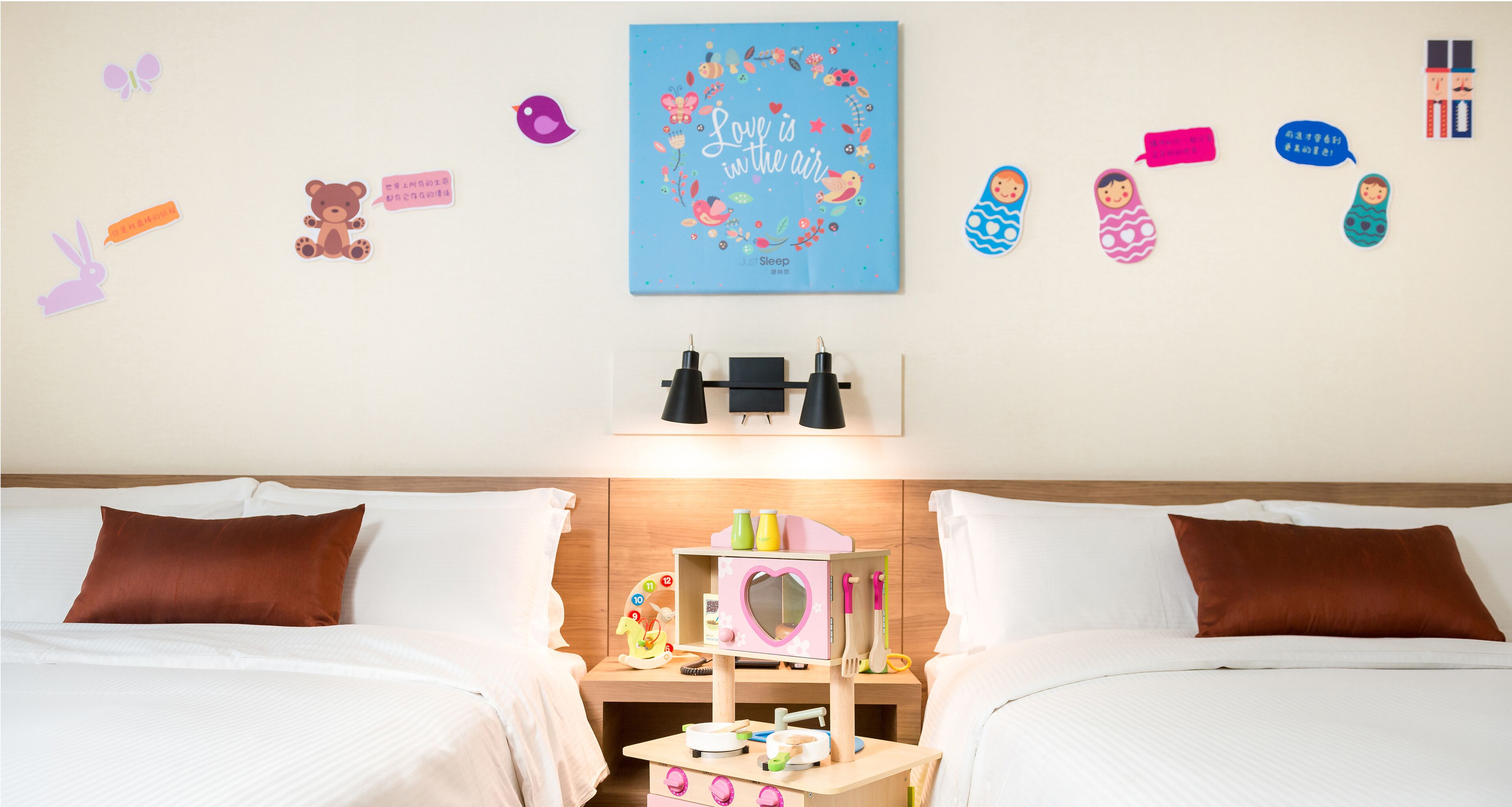 Une chambre d’hôtel conçue pour les enfants, avec deux lits, une table de chevet avec des jouets, une décoration murale et un panneau.