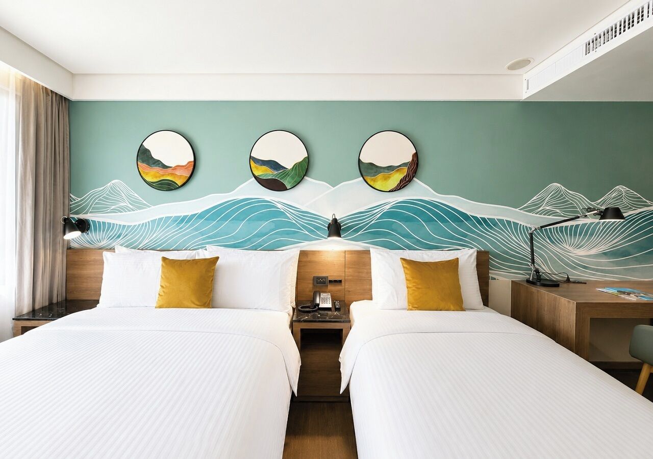 A hotel room with two beds, a desk, and a wall with a wave pattern.