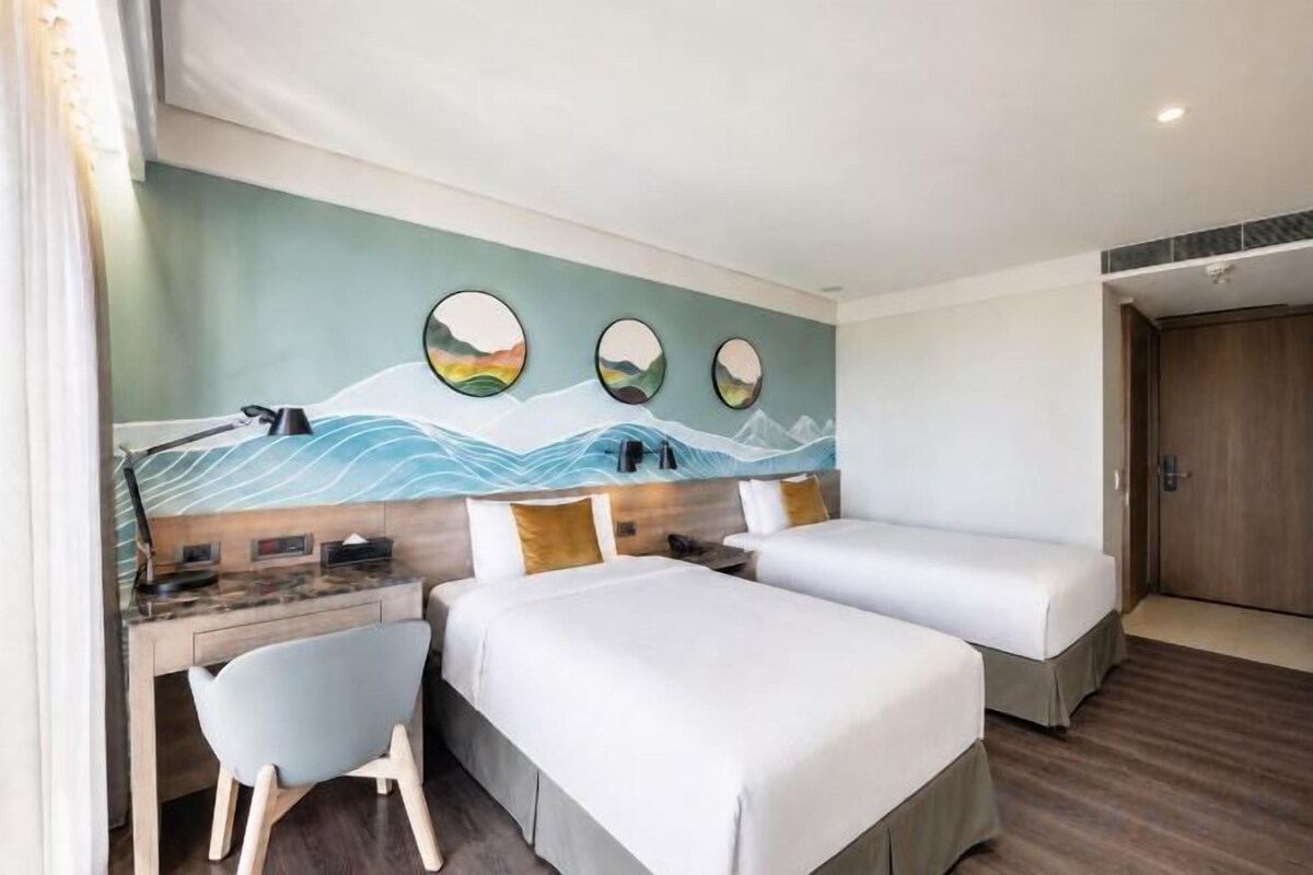 A hotel room with two beds, a desk with a chair, and a wall mural.