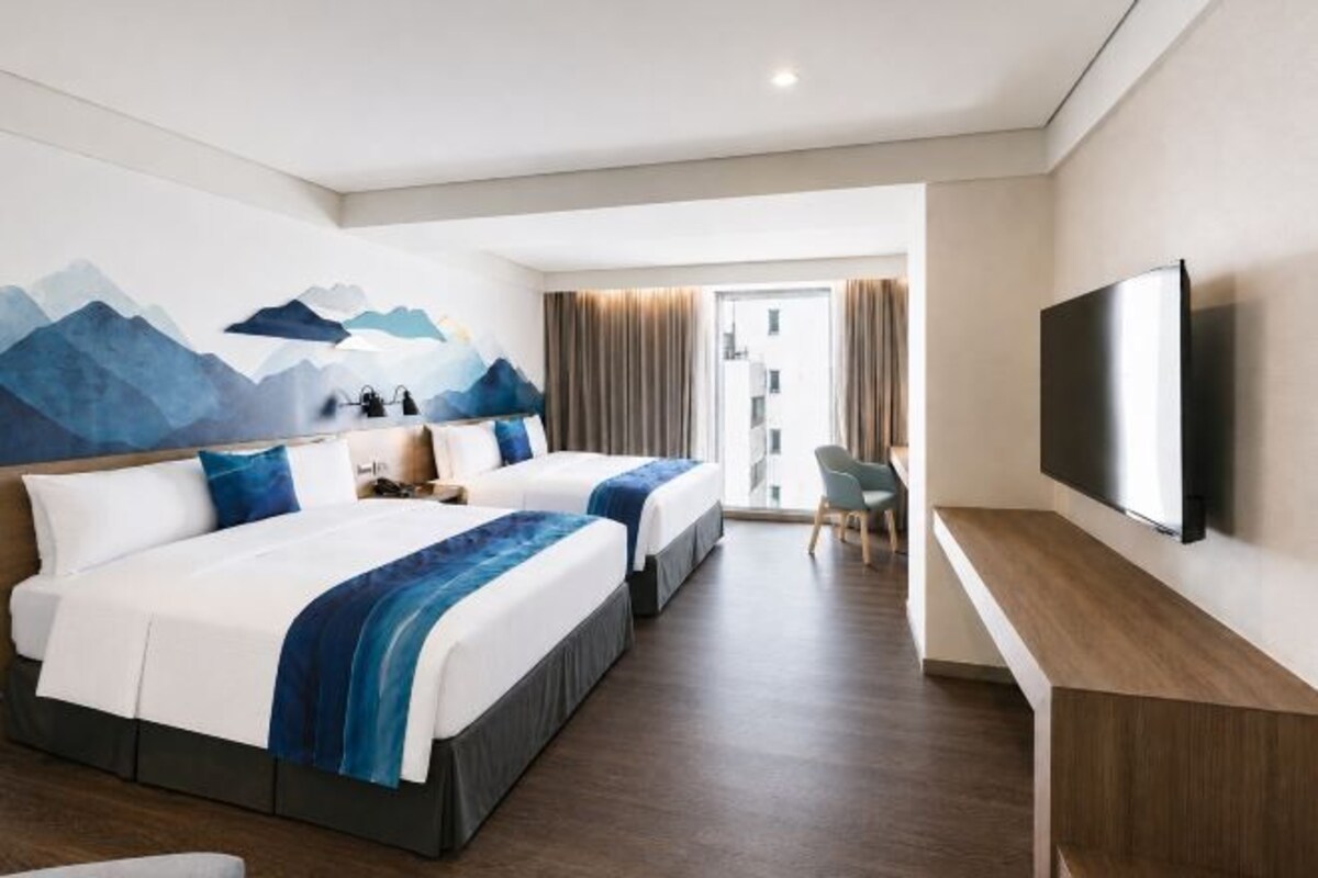 Habitación de hotel con dos camas, un escritorio, un televisor y vistas al exterior.